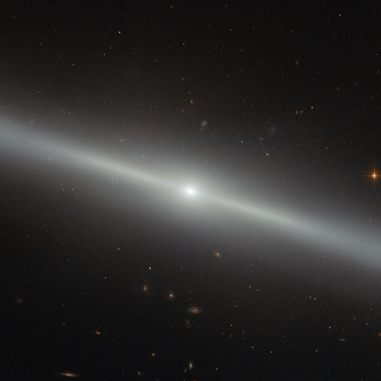 This spectacular image was captured by the NASA/ESA Hubble Space Telescope's Advanced Camera for Surveys (ACS). The bright streak slicing across the frame is an edge-on view of galaxy NGC 4762, and a number of other distant galaxies can be seen scattered in the background. NGC 4762 lies about 58 million light-years away in the constellation of Virgo (The Virgin). It is part of the Virgo Cluster, hence its alternative designation of  VCC 2095 for Virgo Cluster Catalogue entry. This catalogue is a listing of just over 2000 galaxies in the area of the Virgo Cluster. The Virgo Cluster is actually prominently situated, and lies at the centre of the larger Virgo supercluster, of which our galaxy group, the Local Group, is a member. Previously thought to be a barred spiral galaxy, NGC 4762 has since been found to be a lenticular galaxy, a kind of intermediate step between an elliptical and a spiral. The edge-on view that we have of this particular galaxy makes it difficult to determine its true shape, but astronomers have found the galaxy to consist of four main components — a central bulge, a bar, a thick disc and an outer ring. The galaxy's disc is asymmetric and warped, which could potentially be explained by NGC 4762 violently cannibalising a smaller galaxy in the past. The remains of this former companion may then have settled within NGC 4762's disc, redistributing the gas and stars and so changing the disc's morphology. NGC 4762 also contains a Liner-type Active Galactic Nucleus, a highly energetic central region. This nucleus is detectable due to its particular spectral line emission, which acts as a type of "atomic fingerprint", allowing astronomers to measure the composition of the region.